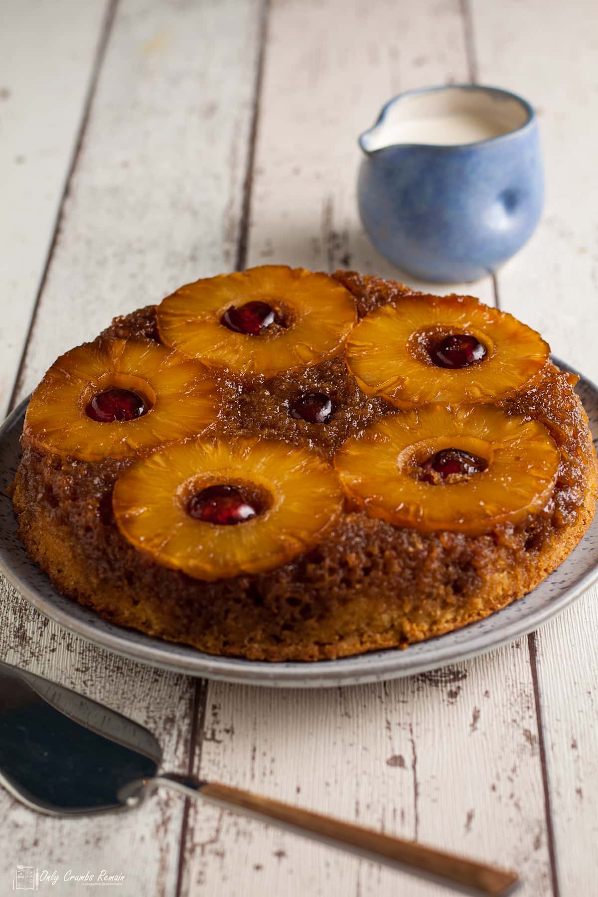 pineapple upside down cake on a plate with cake slice and pot of cream