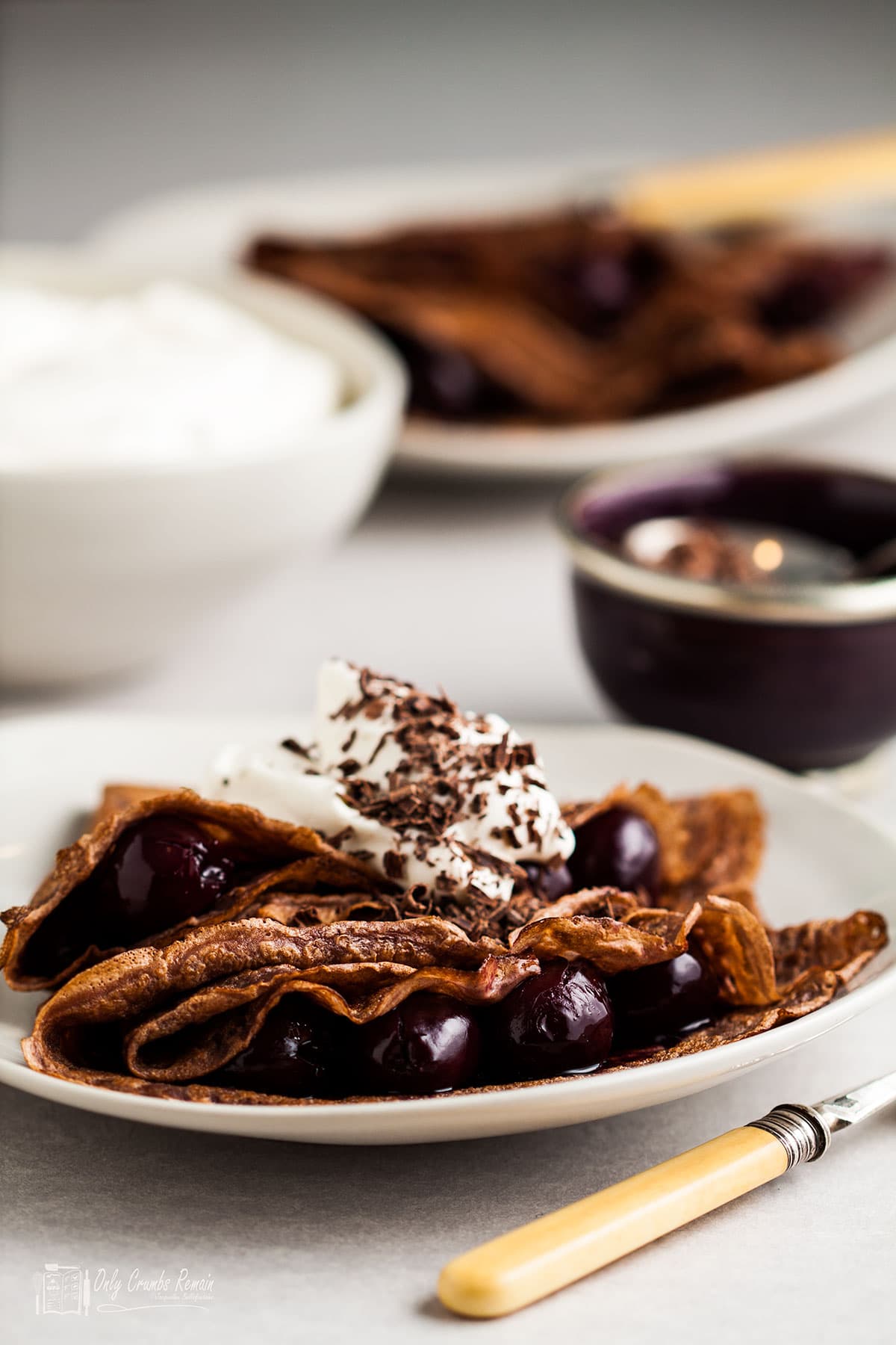 black forest pancakes on a plate with bowl of cream and chocolate behind.